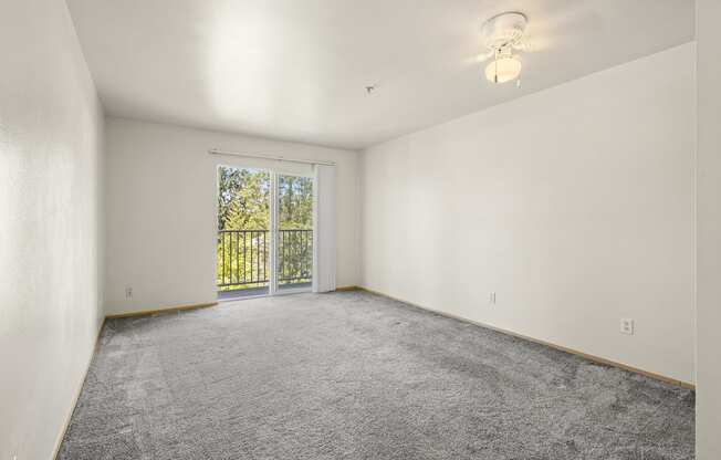 a bedroom with white walls and a sliding glass door to a balcony at Mill Pond Apartments, Auburn Washington