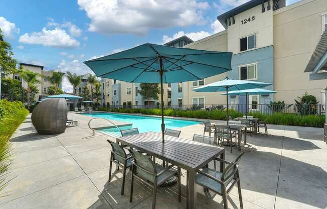 A pool area with a table and chairs and umbrellas.