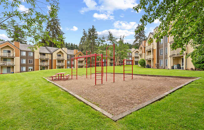A playground with a red swing set in the middle of a grassy area.