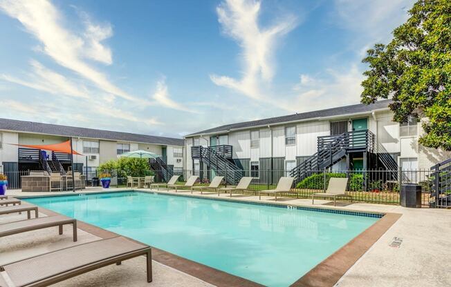 a swimming pool with chaise lounge chairs and trees in front of a building