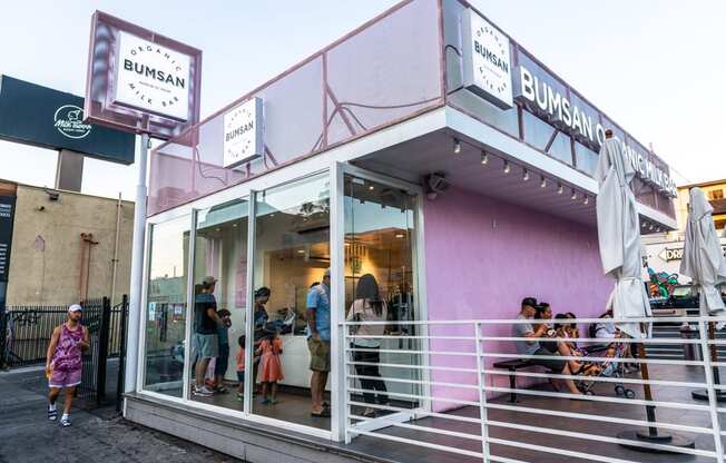 the front of the building is painted purple and white and people are standing and sitting in the