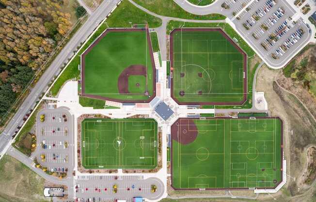 An aerial view of a sports complex with a baseball diamond, soccer fields, and a parking lot.