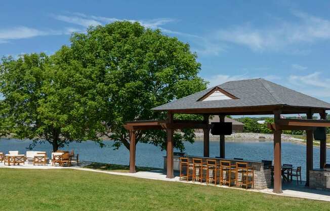 A gazebo with a table and chairs is situated on a lawn by a body of water.