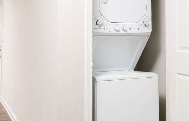 A white washing machine is in a small space between a wall and a door.