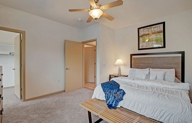A cozy bedroom here at Swan Creek with plush carpet, warm wood trim, ceiling fan, and bright lighting, creating a comfortable, inviting, and relaxing space with convenient closet access.