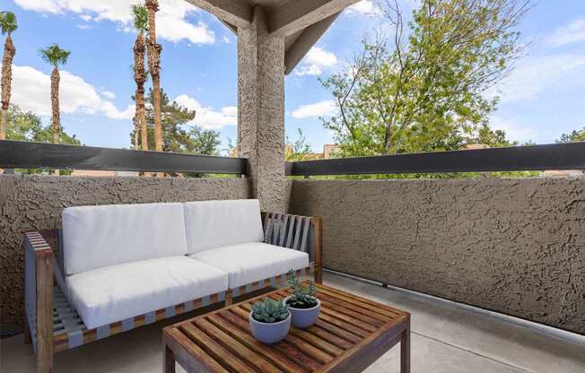 A wooden sofa with white cushions sits on a patio with a wooden table in front of it.
