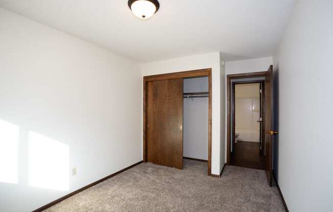 a room with a carpeted floor and a door to a closet and a hallway. Fargo, ND Country Club Apartments