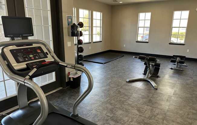 A treadmill with a monitor and control panel is in a spacious gym with other exercise equipment.