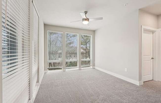 A large bedroom with floor to ceiling windows all through out the room,  a ceiling fan