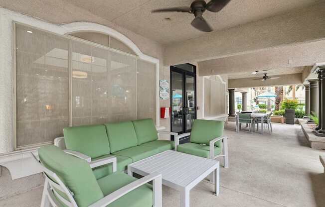 A white patio with green cushions and a fan.