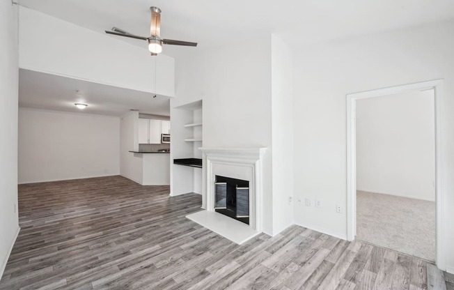 A living room with a fireplace, a ceiling fan, and shelving with a desk area.