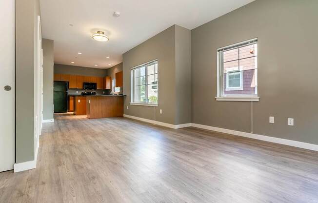 A spacious living room with wood flooring and a kitchen area in the background.