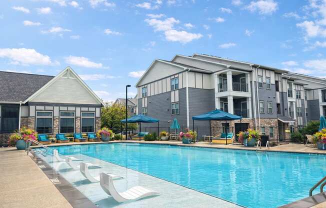 A swimming pool surrounded by lounge chairs and umbrellas in front of a building.