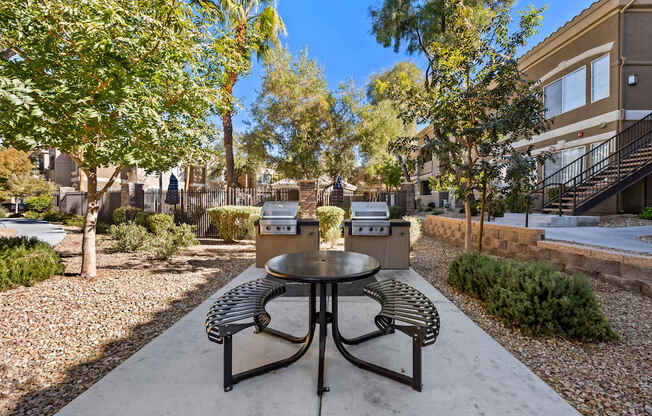 A table and chairs set in a courtyard with a tree and a building in the background.