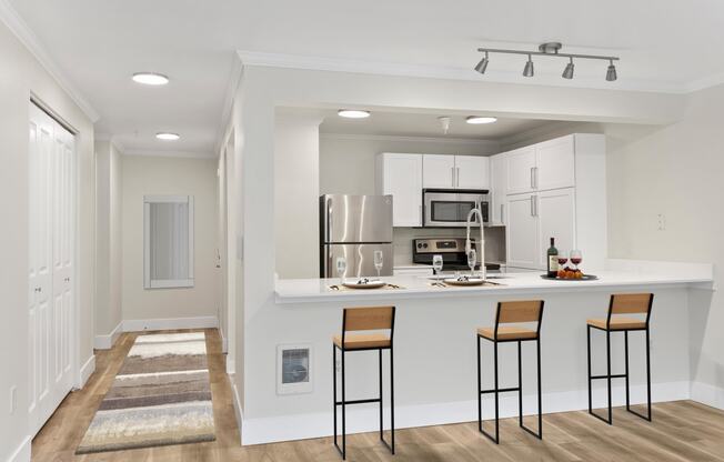 a kitchen with a breakfast bar, bar stool, white cabinetry and stainless appliances