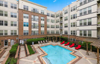 A large swimming pool surrounded by red chairs and apartment buildings.