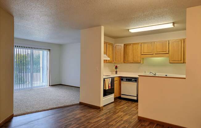 A living room with a glass sliding door and kitchen. Fargo, ND Flagstone Apartments.
