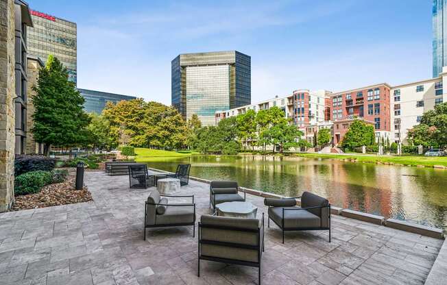 A park with chairs and a pond in the foreground and buildings in the background.