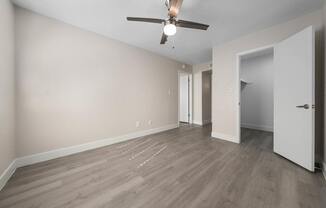 A room with a ceiling fan and light fixture, hardwood flooring, and white walls.