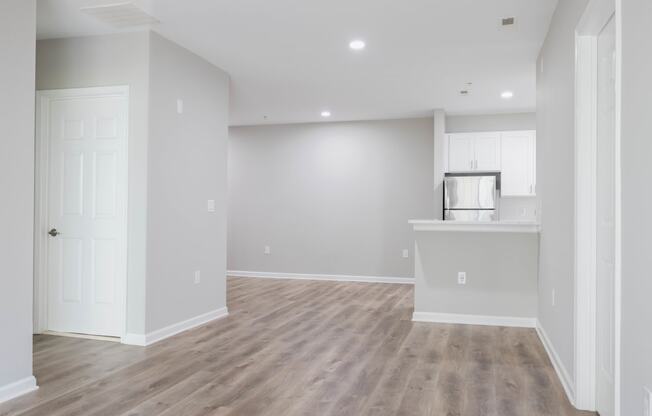 an empty living room and kitchen with white walls and wood flooring