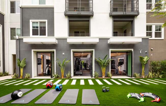 A yoga mat and exercise equipment are placed on a green lawn in front of a building.