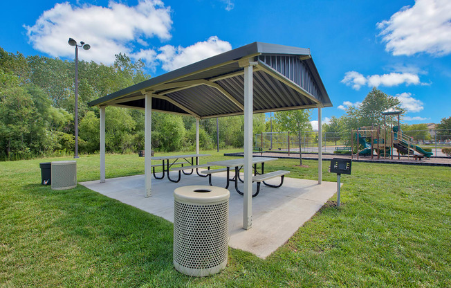 a picnic shelter with a table and benches in a park with a playground in the background at Evergreen Luxury Apartments, Indiana, 46410