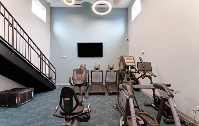 A gym with a row of treadmills and elliptical machines.