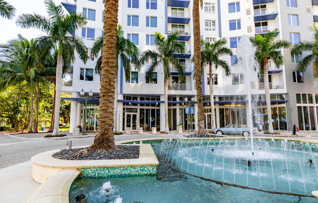 a fountain in front of a building with palm trees