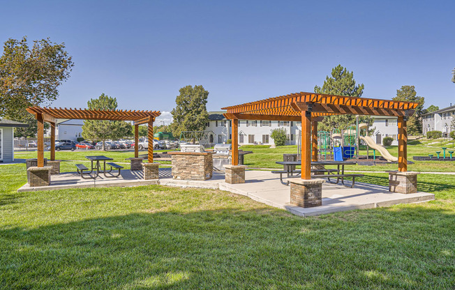 a picnic area with benches and a pergola in the middle of a grassy area