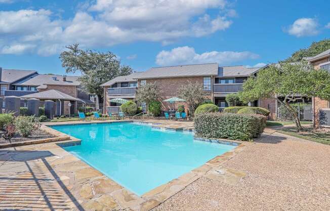 A swimming pool surrounded by a stone border and a residential area.