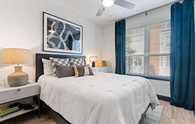 A bedroom with a large bed, a nightstand with a lamp, and a picture on the wall.