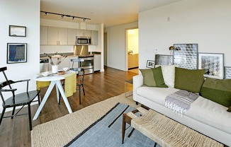 Open layout living space that flows into a dining and kitchen area. Staged with a couch, coffee table, circular dining table and dining chairs.at 19th & Mercer, Seattle, WA 98112