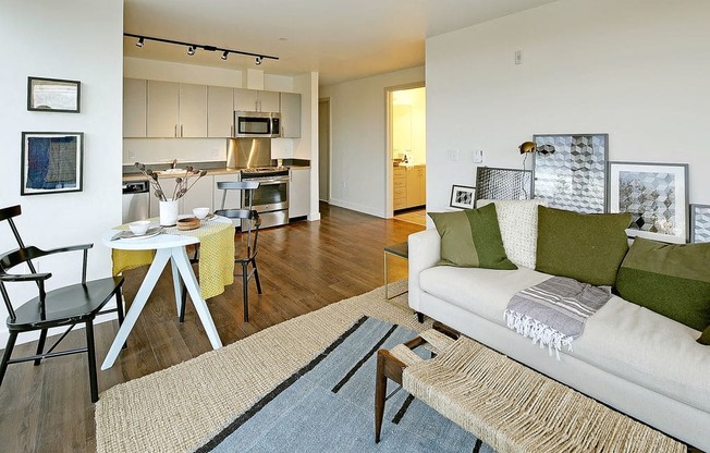 Open layout living space that flows into a dining and kitchen area. Staged with a couch, coffee table, circular dining table and dining chairs.at 19th & Mercer, Seattle, WA 98112