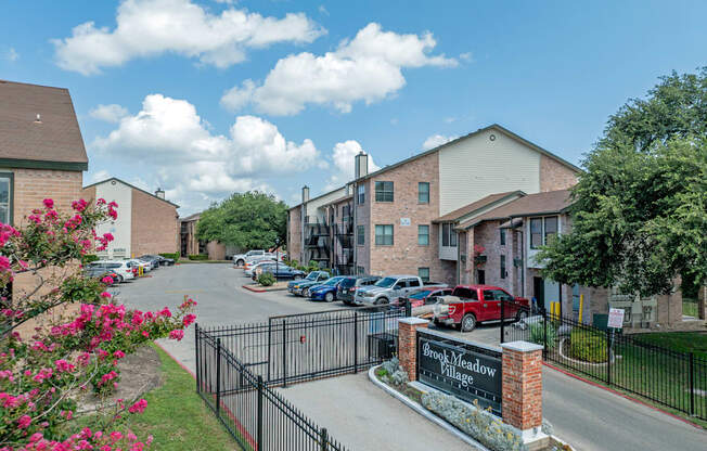 A sign that says Brook Meadow Village is in front of a gated parking lot.