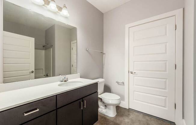 A white toilet sits in a bathroom with a white sink and a white door.
