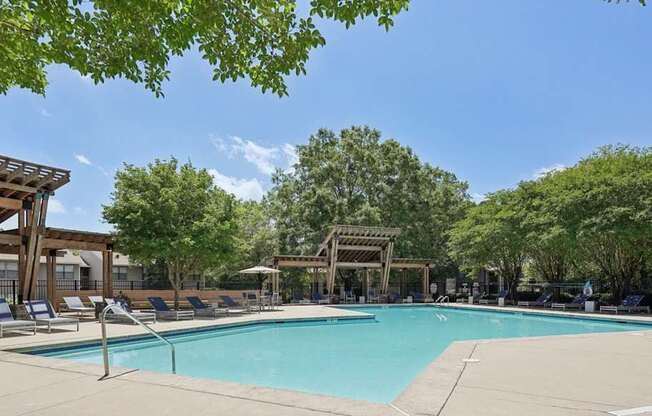 A large swimming pool surrounded by trees and a wooden pergola.