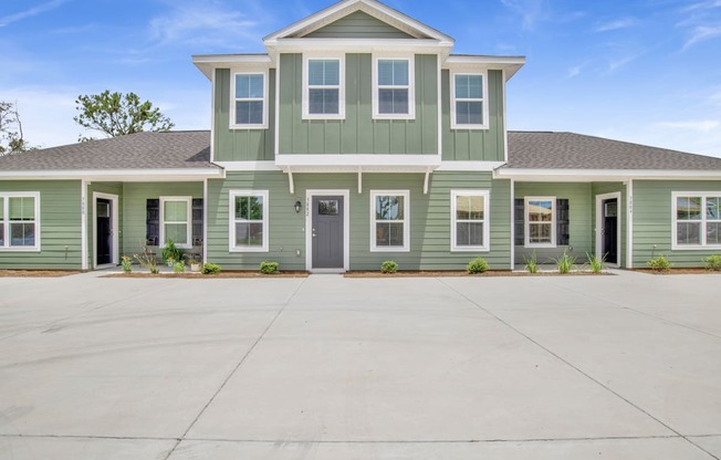 a green house with a large driveway in front of it