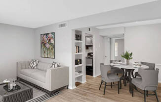 A living room with a white couch and a dining table with grey chairs.