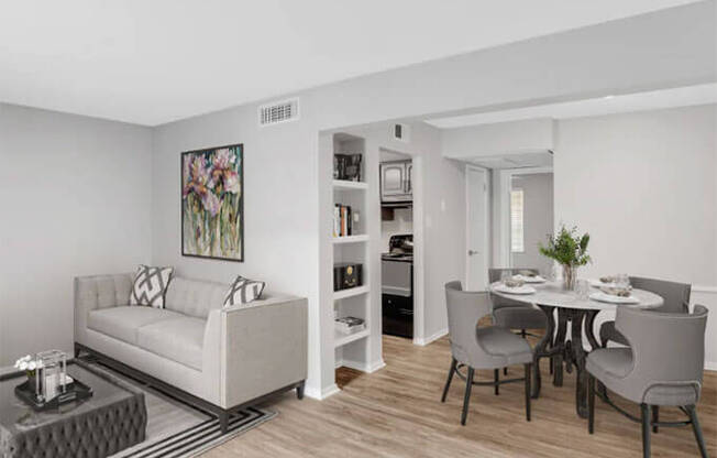 A living room with a white couch and a dining table with grey chairs.