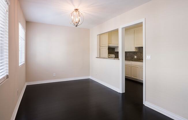 an empty living room with dark wood flooring and a kitchen