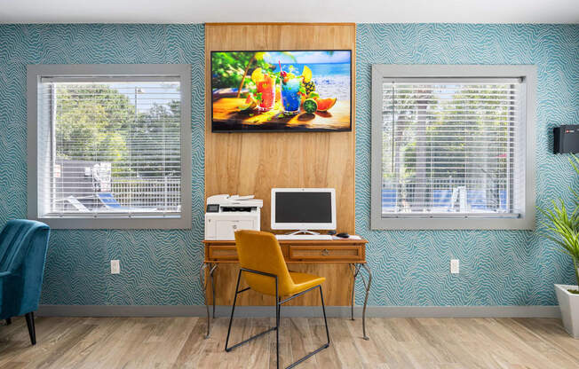 a computer desk with a yellow chair and a painting on the wall