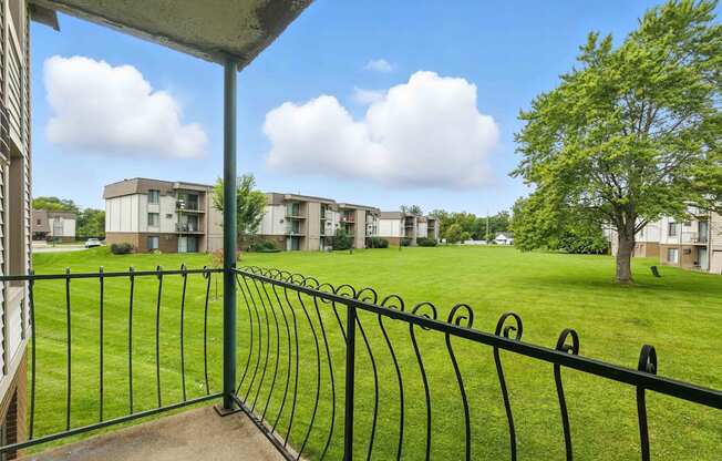 A view from a balcony overlooking a grassy area with apartment buildings in the distance.