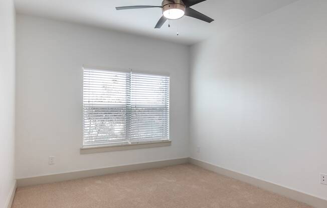 A room with a ceiling fan and a window with blinds.