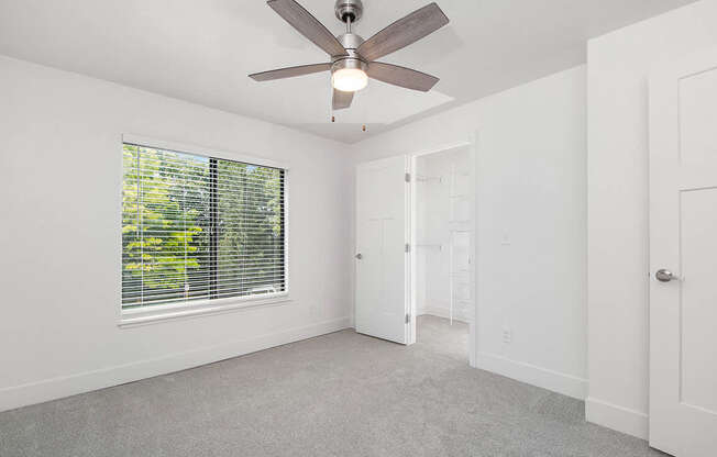 A bedroom with a ceiling fan and a window with blinds at The Crossings Apartments, Grand Rapids, Michigan