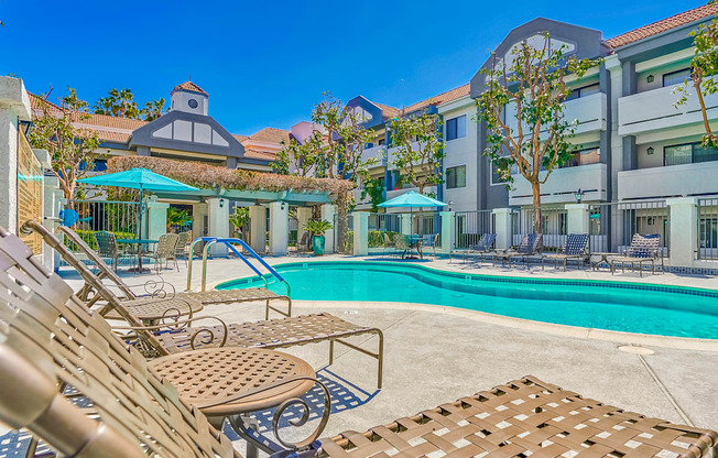 a swimming pool with lounge chairs and umbrellas in front of a building