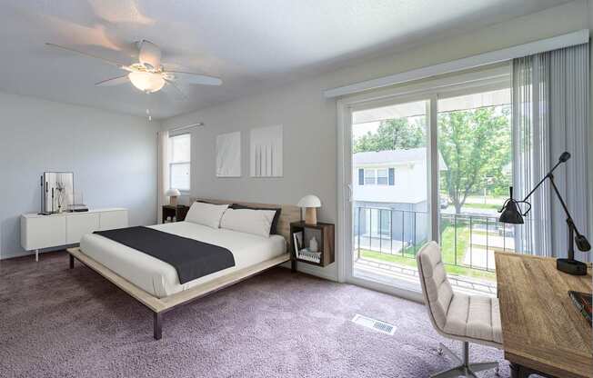 A bedroom with a large bed and a balcony view at Spring Creek Townhomes Apartments, Springfield, IL