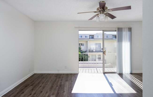 an empty living room with a ceiling fan and a balcony