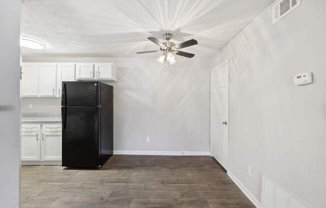 A black fridge in the kitchen leading to a dining area with a ceiling fan at Gwinnett Square Apartments in Duluth, GA