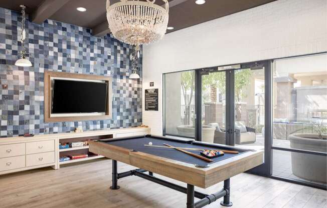 A pool table is in the middle of a room with a tv and a chandelier.