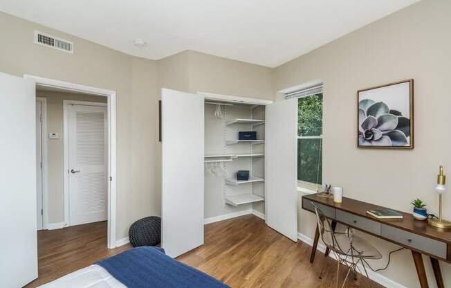 A room with a desk, chair, and a bed with a blue blanket.